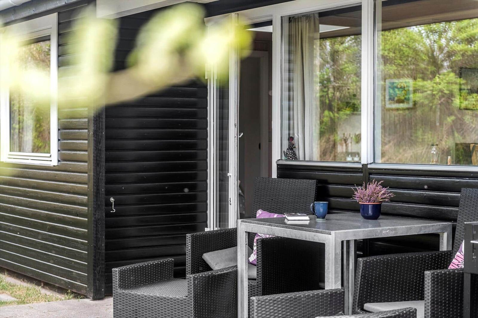 Außenbereich mit Tisch und Stühlen vor einem Haus mit schwarzem Holzschindelverkleidung.