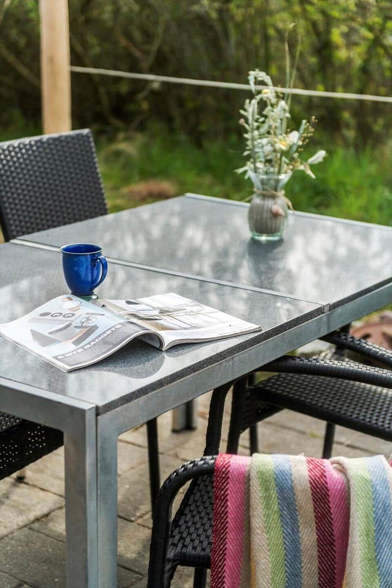 Außentisch mit Stühlen, Tasse, Zeitschrift und Blumenarrangement.