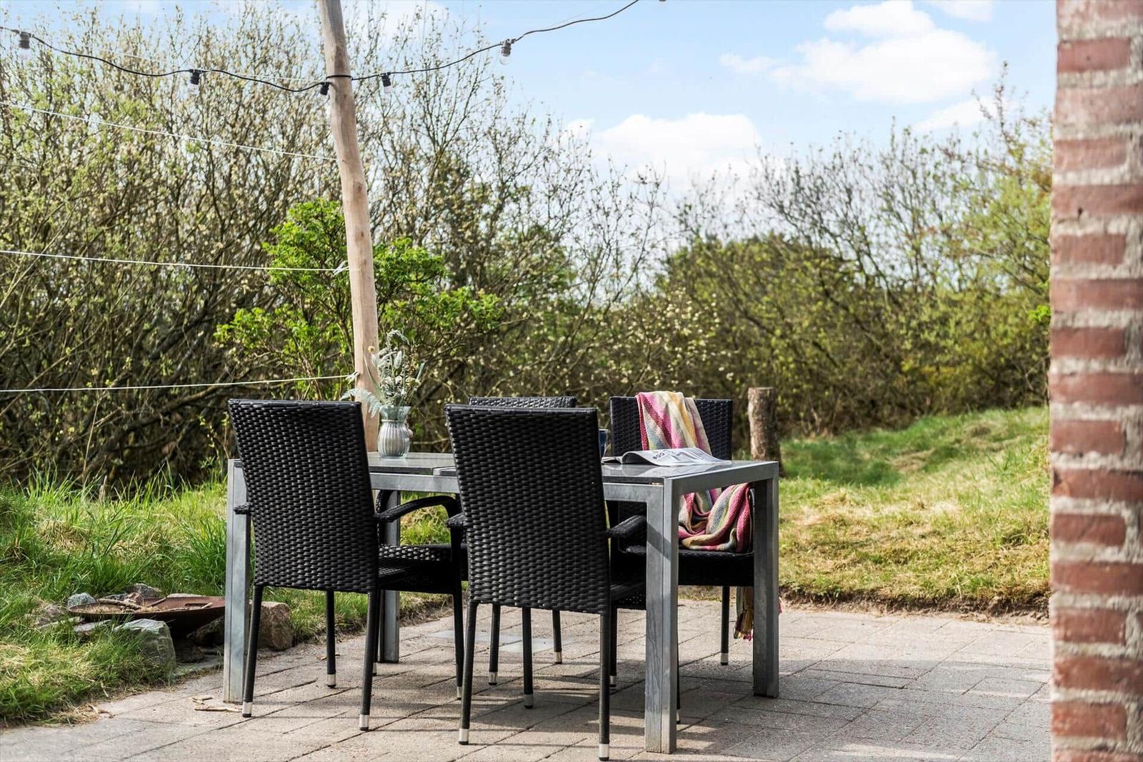 Außenbereich mit Tisch und Stühlen, umgeben von Grün und einem Steinweg.