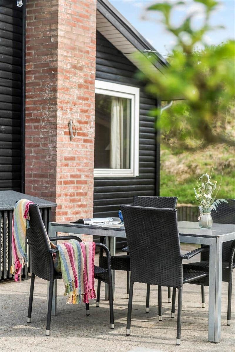 Terrasse mit Tisch und Stühlen, roter Ziegelsockel, grüne Vegetation im Hintergrund.