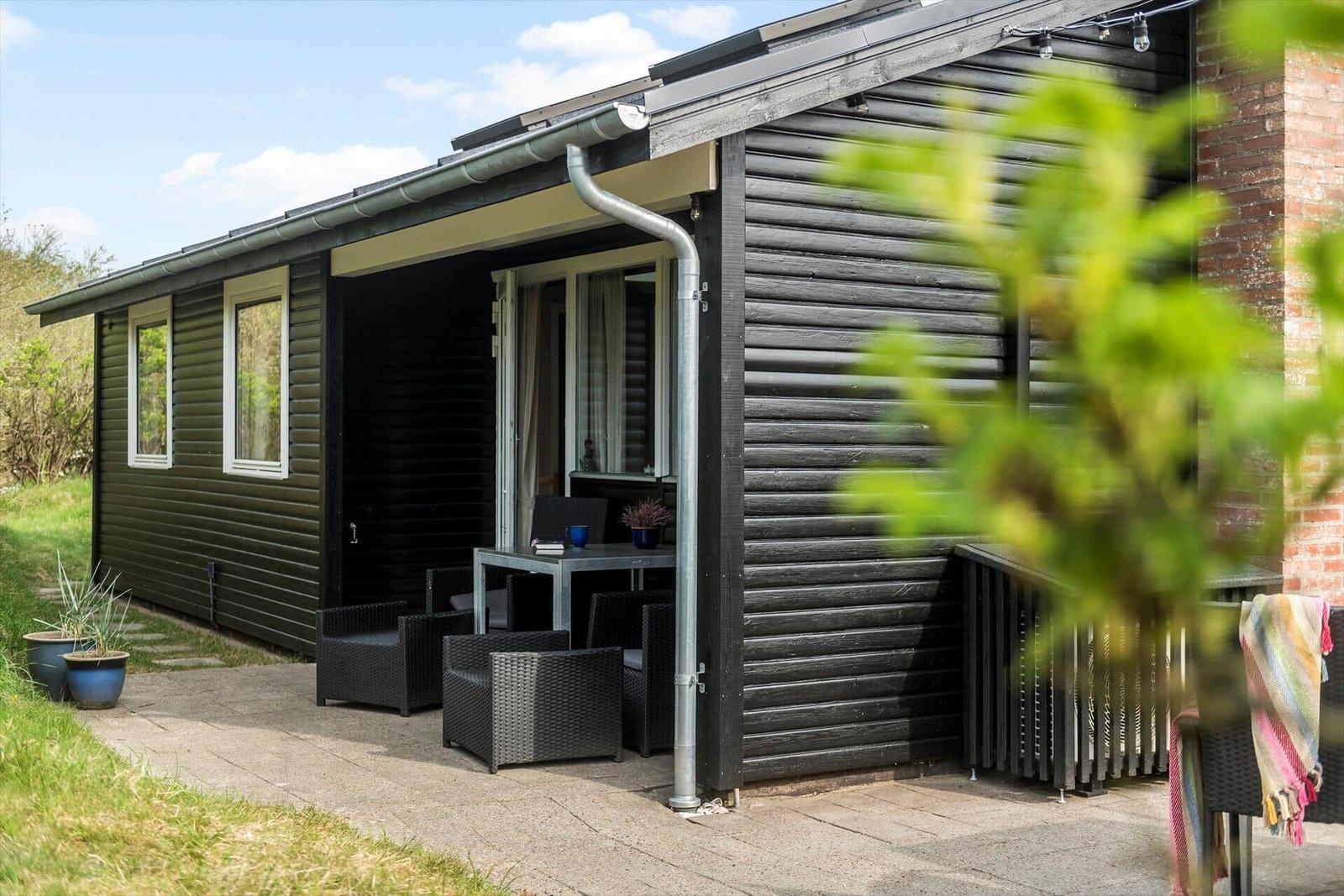Holzhaus mit Terrasse, Sitzgruppe und Pflanzen im Garten.