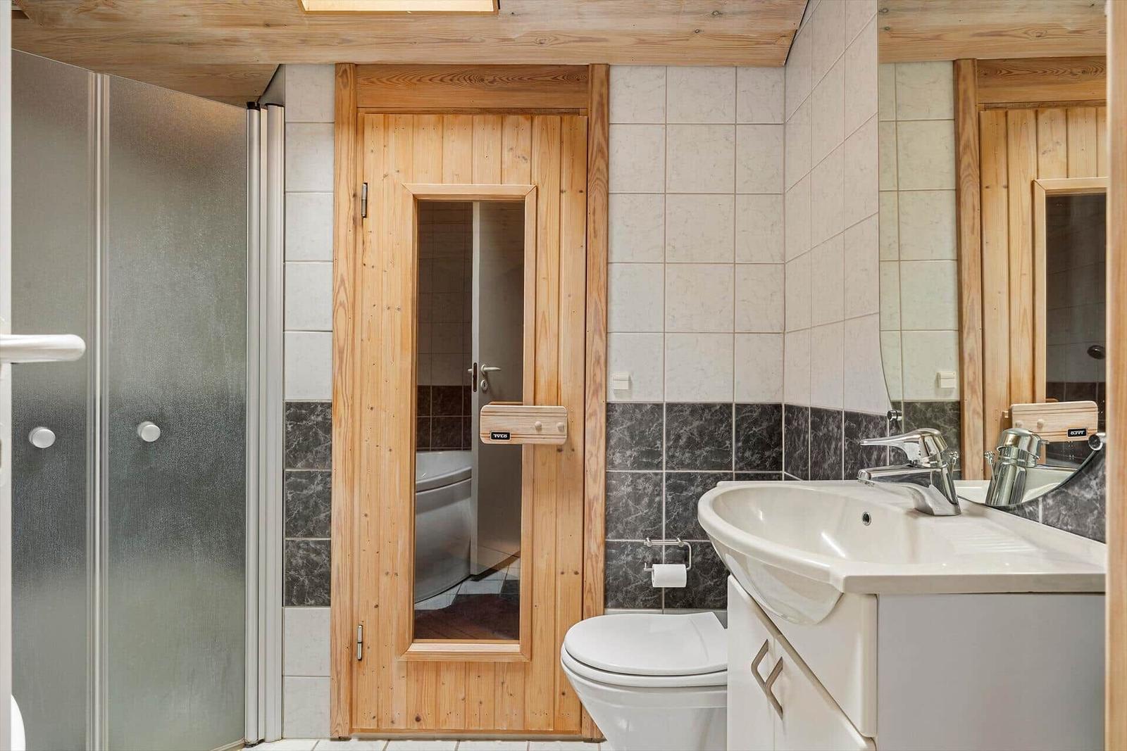 Bad mit Dusche, WC und Waschbecken. Holztür führt in die Badewanne.