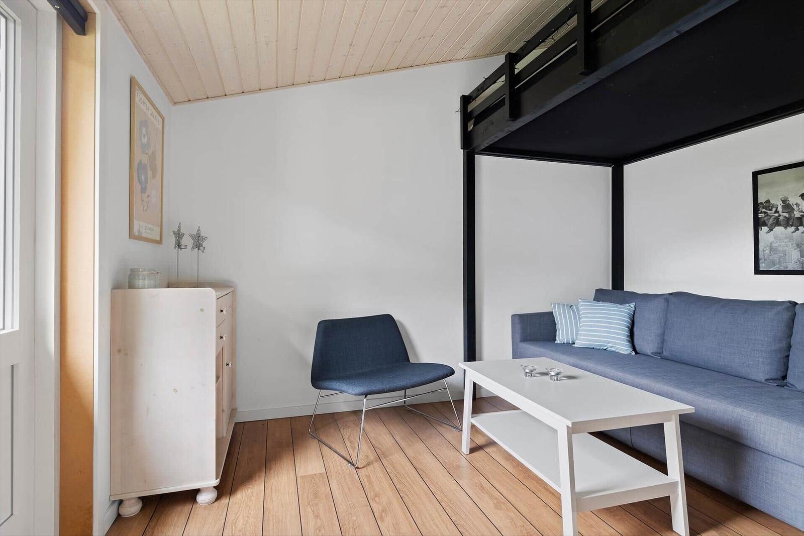 Wohnraum mit Sofa, Stuhl und Couchtisch. Obergeschoss mit Schlafplatz.