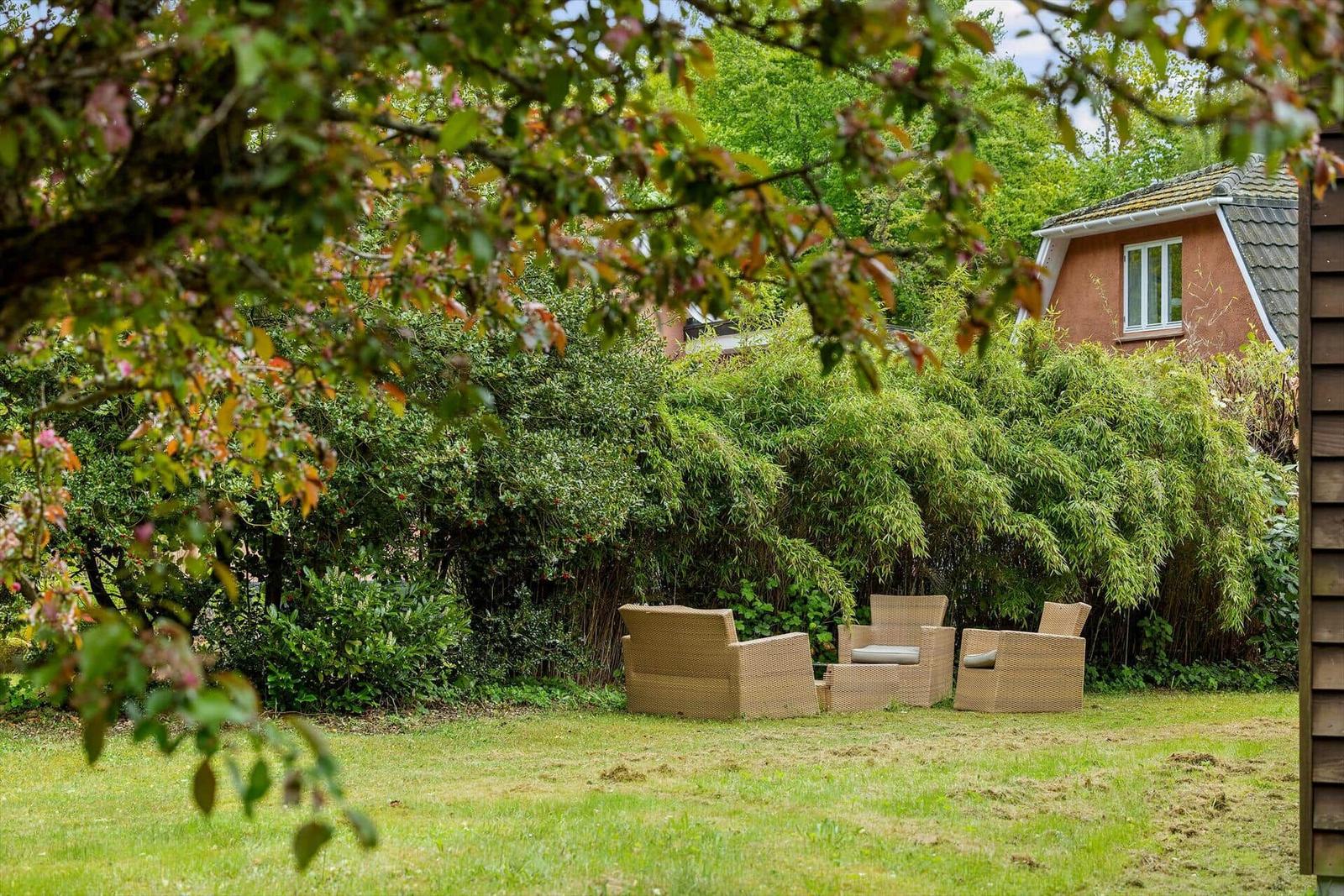 Garten mit drei Rattan-Sitzgelegenheiten und grüner Vegetation im Hintergrund.