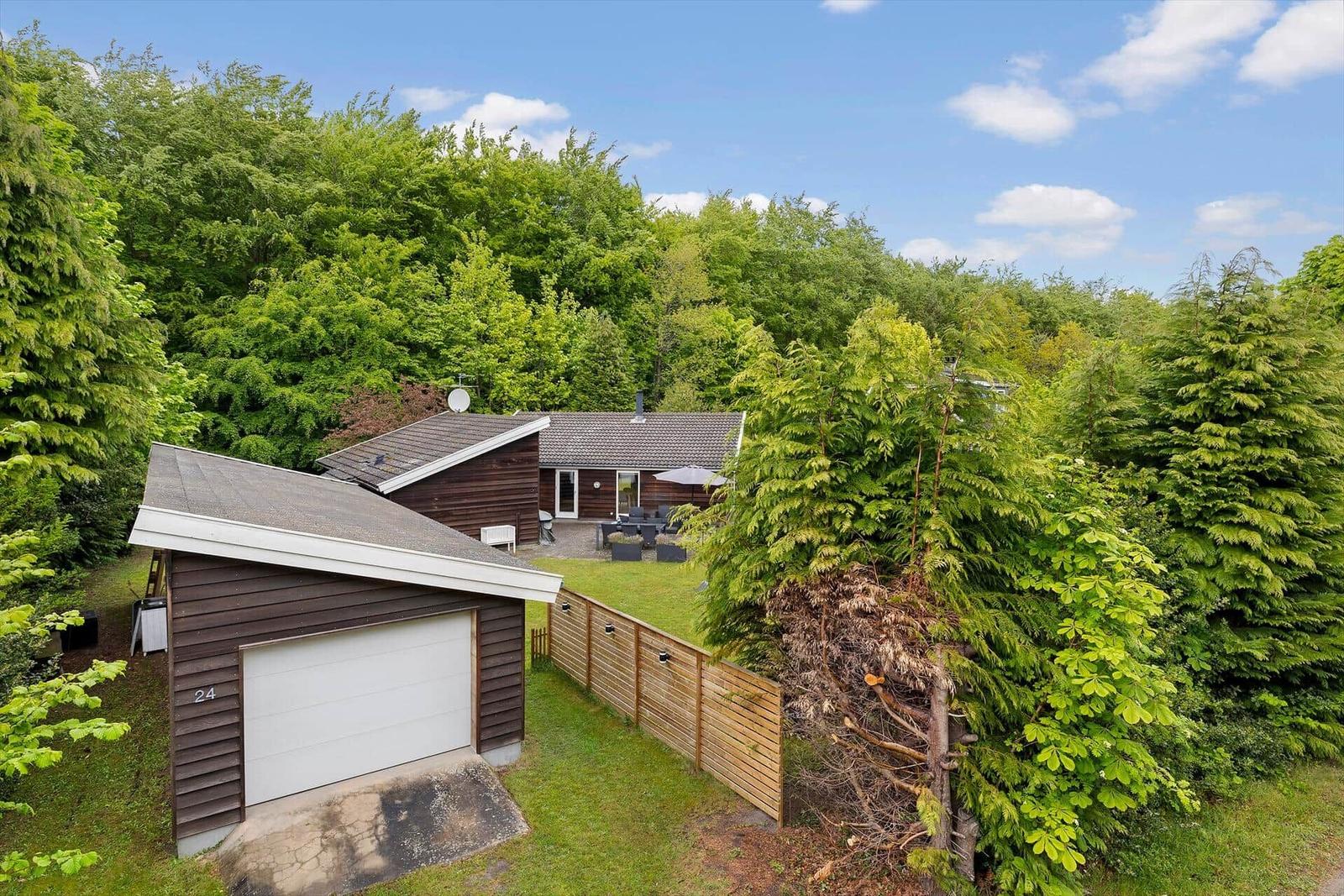 Haus mit Garage und Garten, umgeben von Bäumen unter blauem Himmel.