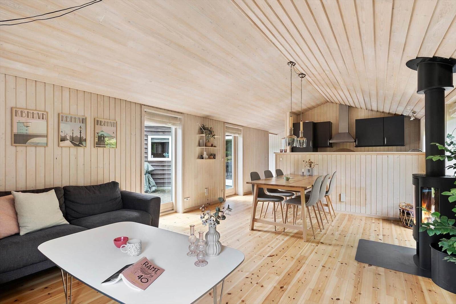 Wohn- und Essbereich mit Holzdecke, Sofa, Tisch und Kaminofen.