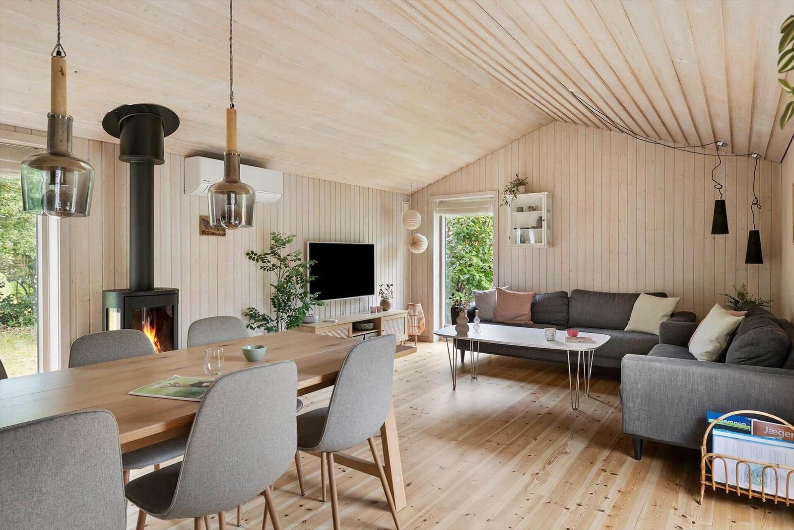 Wohn- und Essbereich mit Holzdecke, Sofa, Esstisch und Kamin.