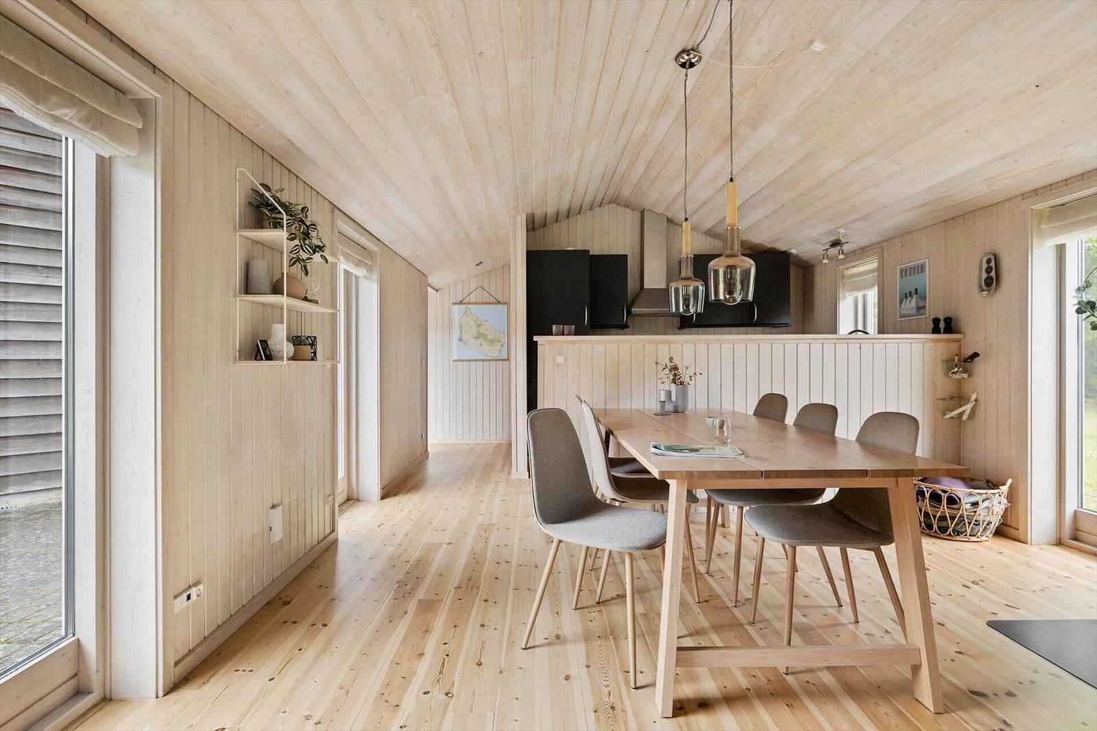 Essbereich mit Holztisch und Stühlen. Küchenbereich im Hintergrund. Holzwände und -boden.