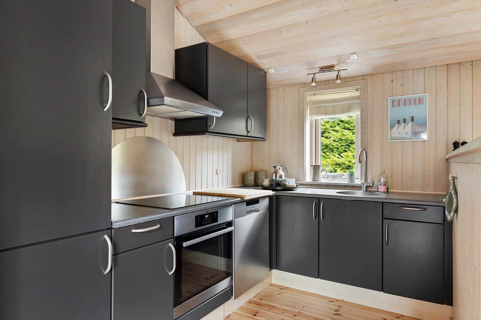 Küche mit dunklen Schränken, Edelstahlgeräten und Holzwandverkleidung.