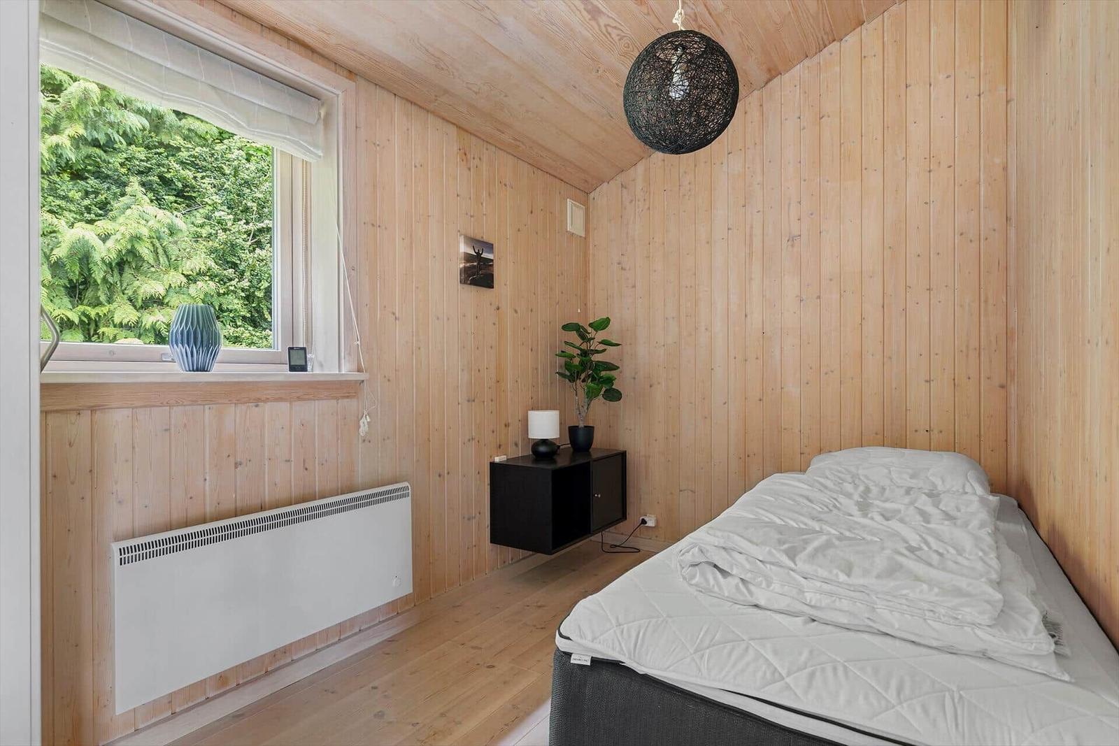 Schlafzimmer mit Holzwand, Bett, Fenster und Pflanze.