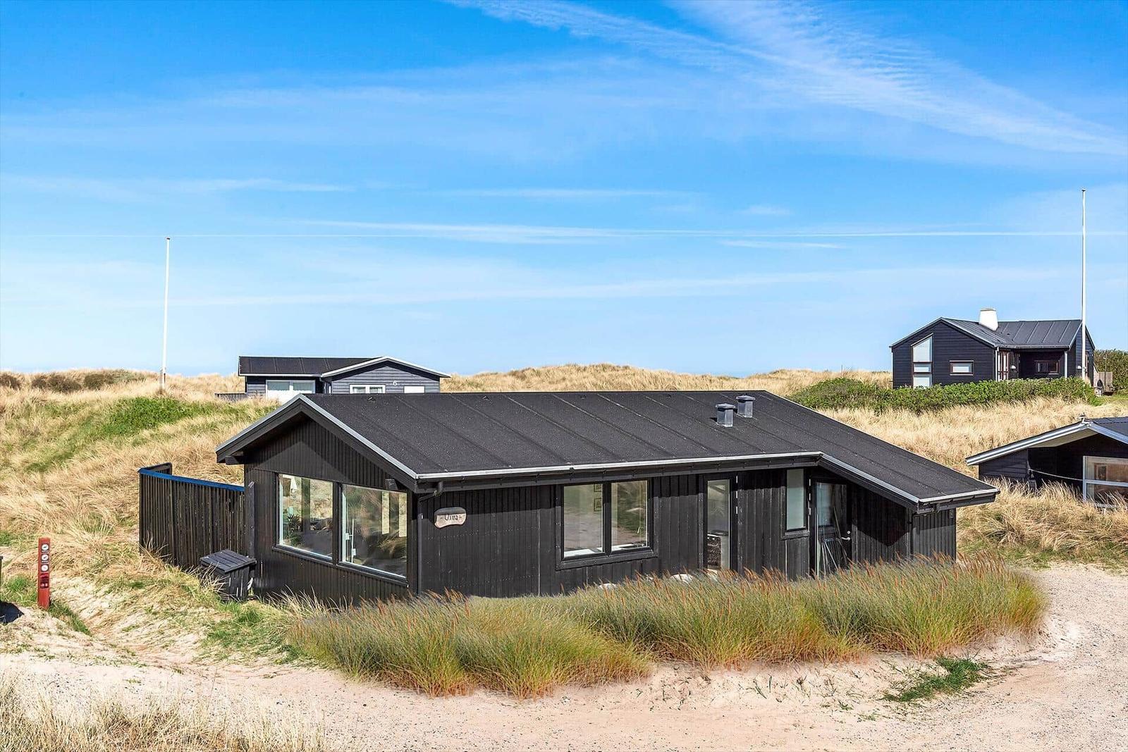 Schwarzes Strandhaus mit großen Fenstern zwischen Dünen.