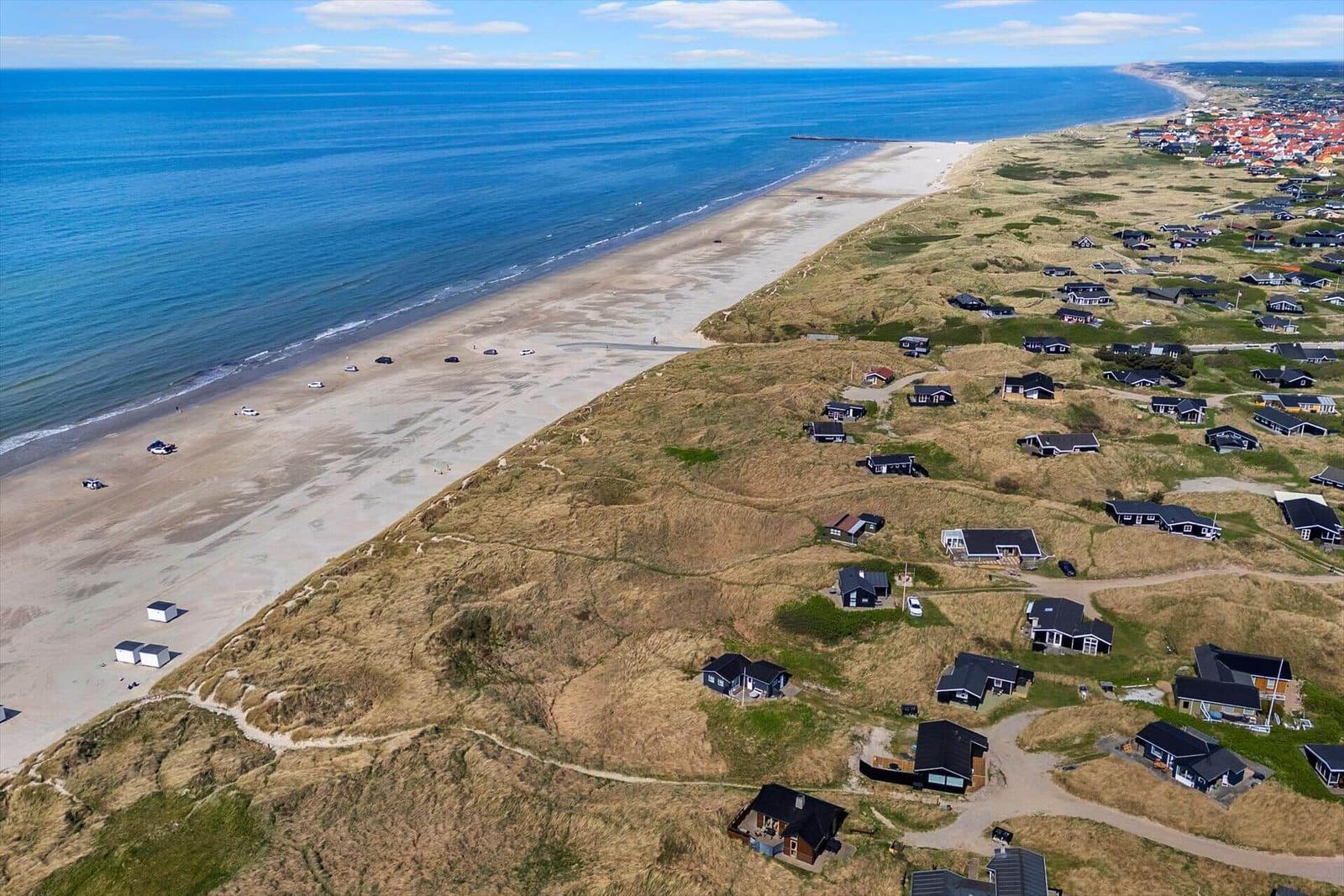Aussicht auf Strand, Dünen und Ferienhäuser entlang der Küste.