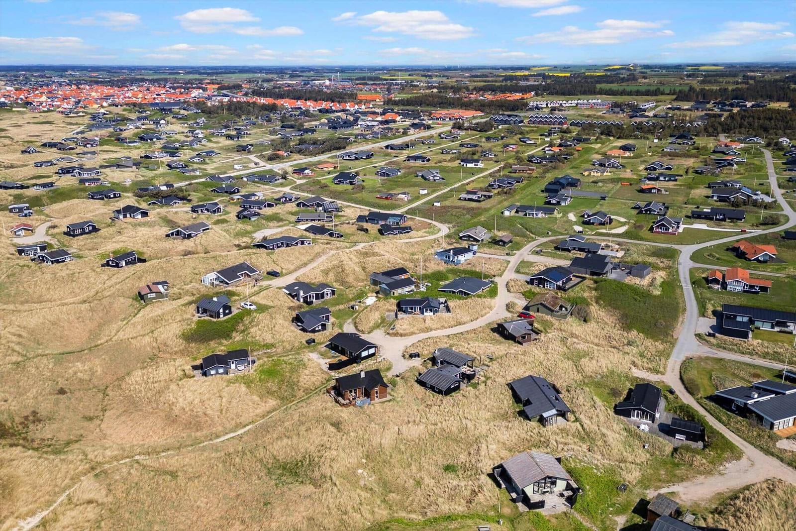 Aerial view of holiday homes on dunes near a town.