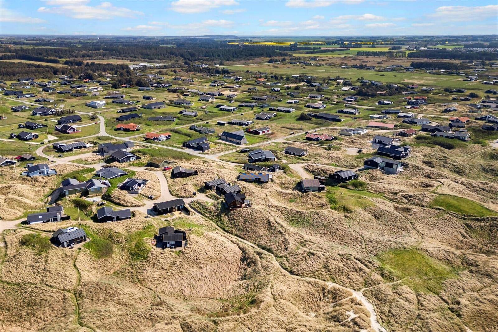 Luftaufnahme von Ferienhäusern auf Dünen mit grünen Feldern im Hintergrund.