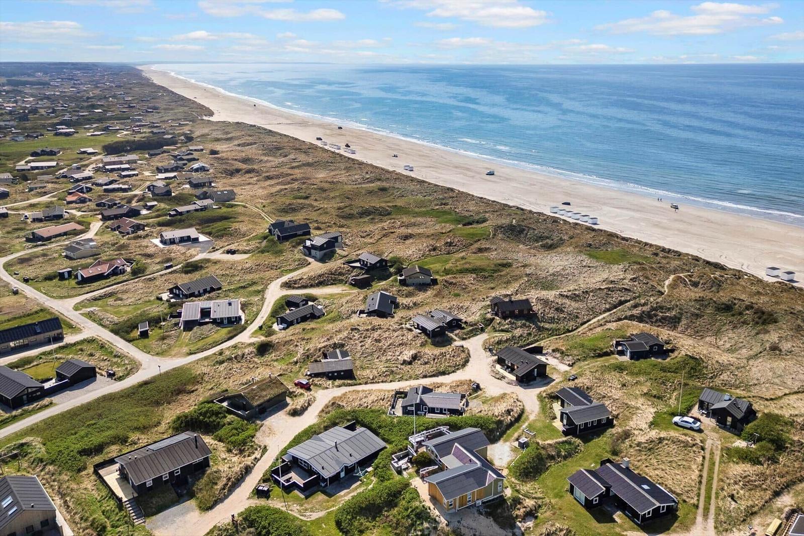 Aerial view of beachside houses on dunes near ocean.