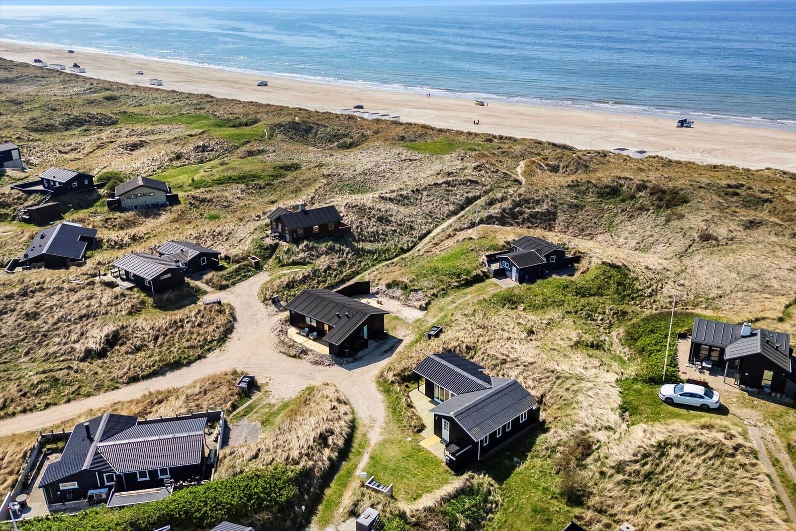 Hütten auf Dünen überblicken einen Sandstrand und das Meer.