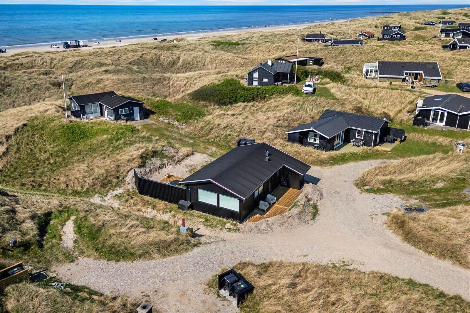 Meerblick auf moderne Häuser in Dünenlandschaft mit Strand im Hintergrund.