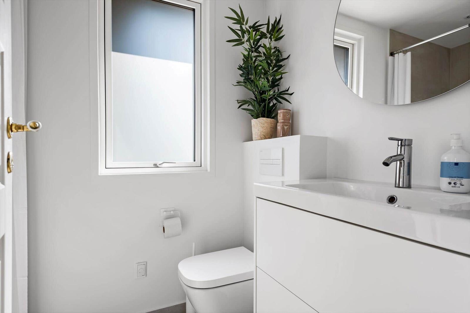 Badezimmer mit Waschbecken, Spiegel, Toilette und Pflanze.
