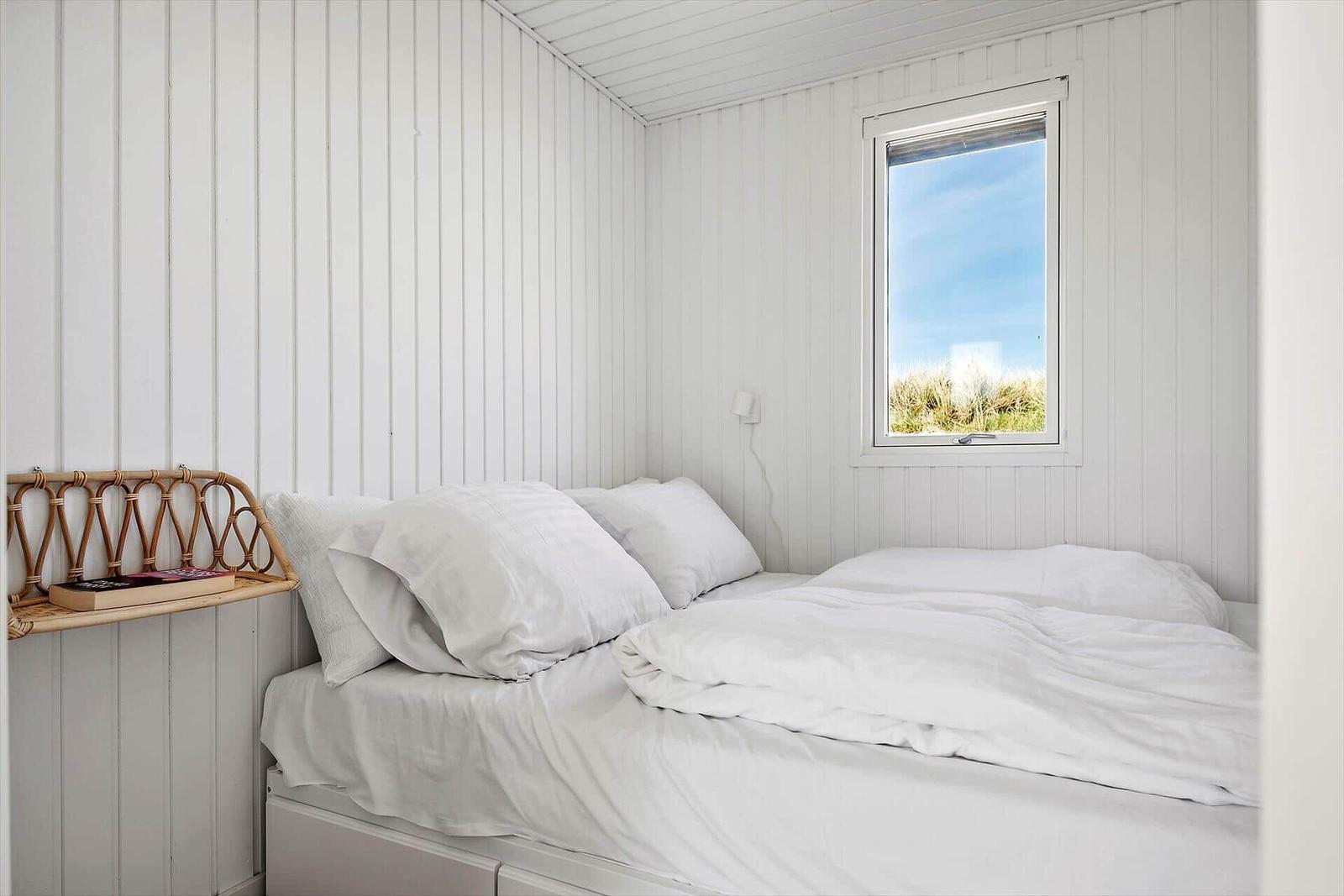 Schlafzimmer mit weißem Bett und Fensterblick auf Gras.