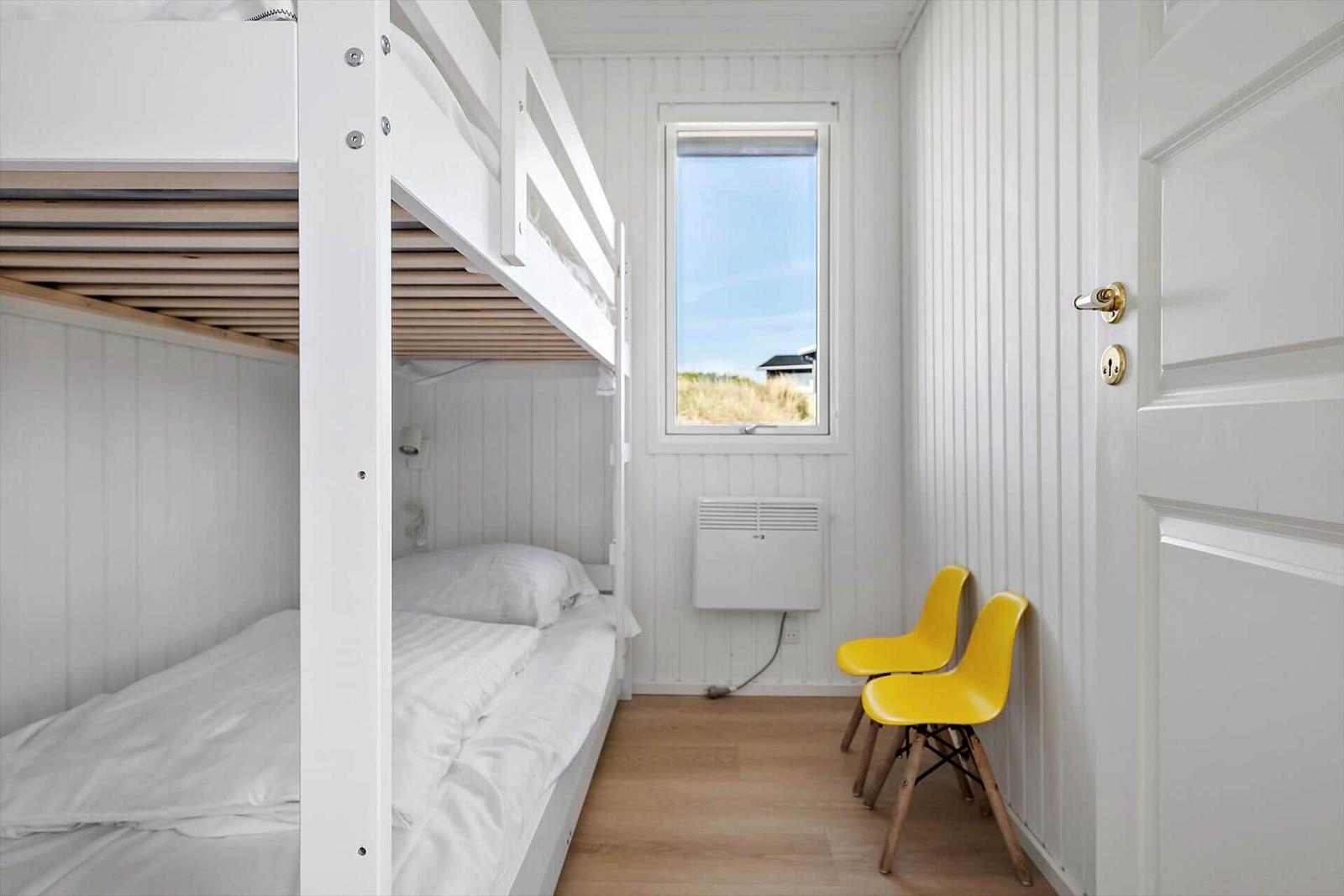 Zimmer mit Doppelstockbett, Fenster und zwei gelben Stühlen.