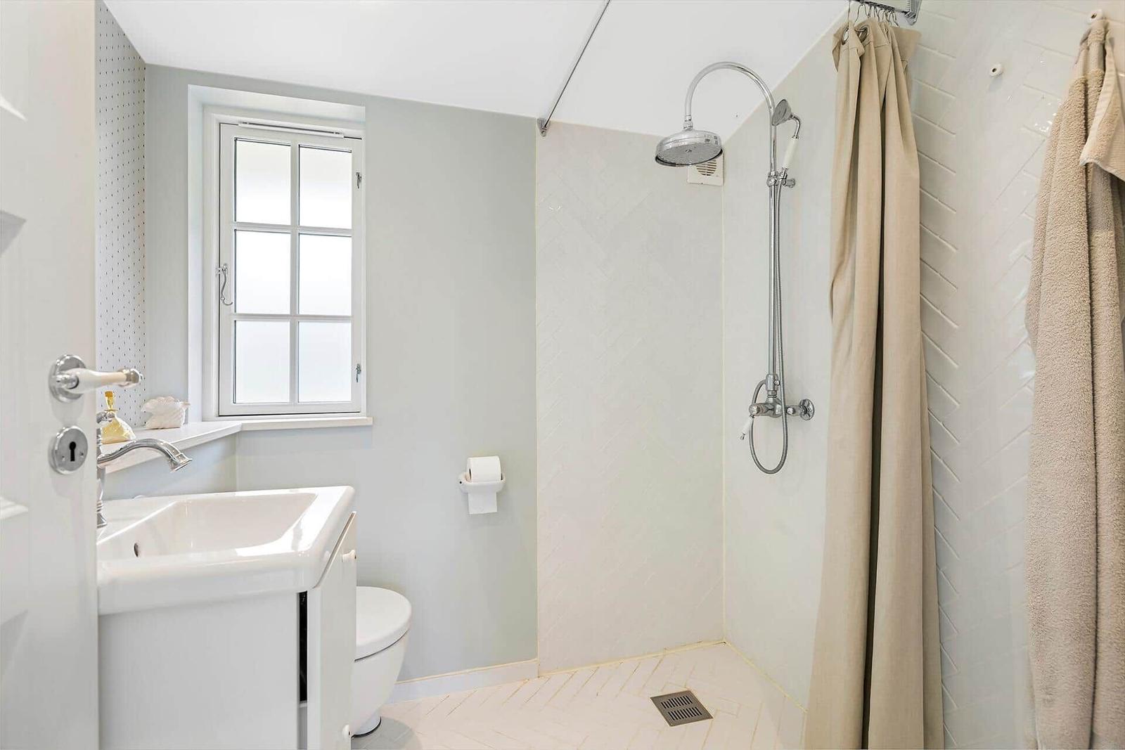 Bathroom with shower, toilet, and sink. Window and light tiled floor.