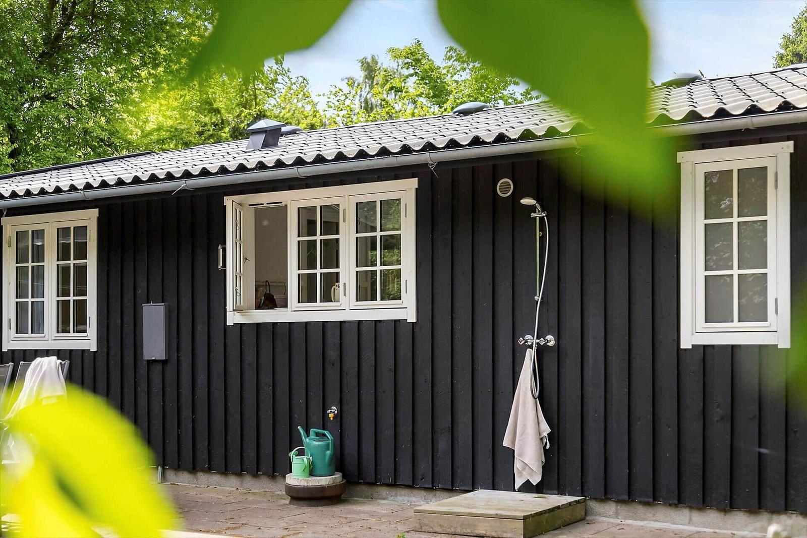 Black wooden house with white windows and outdoor shower.