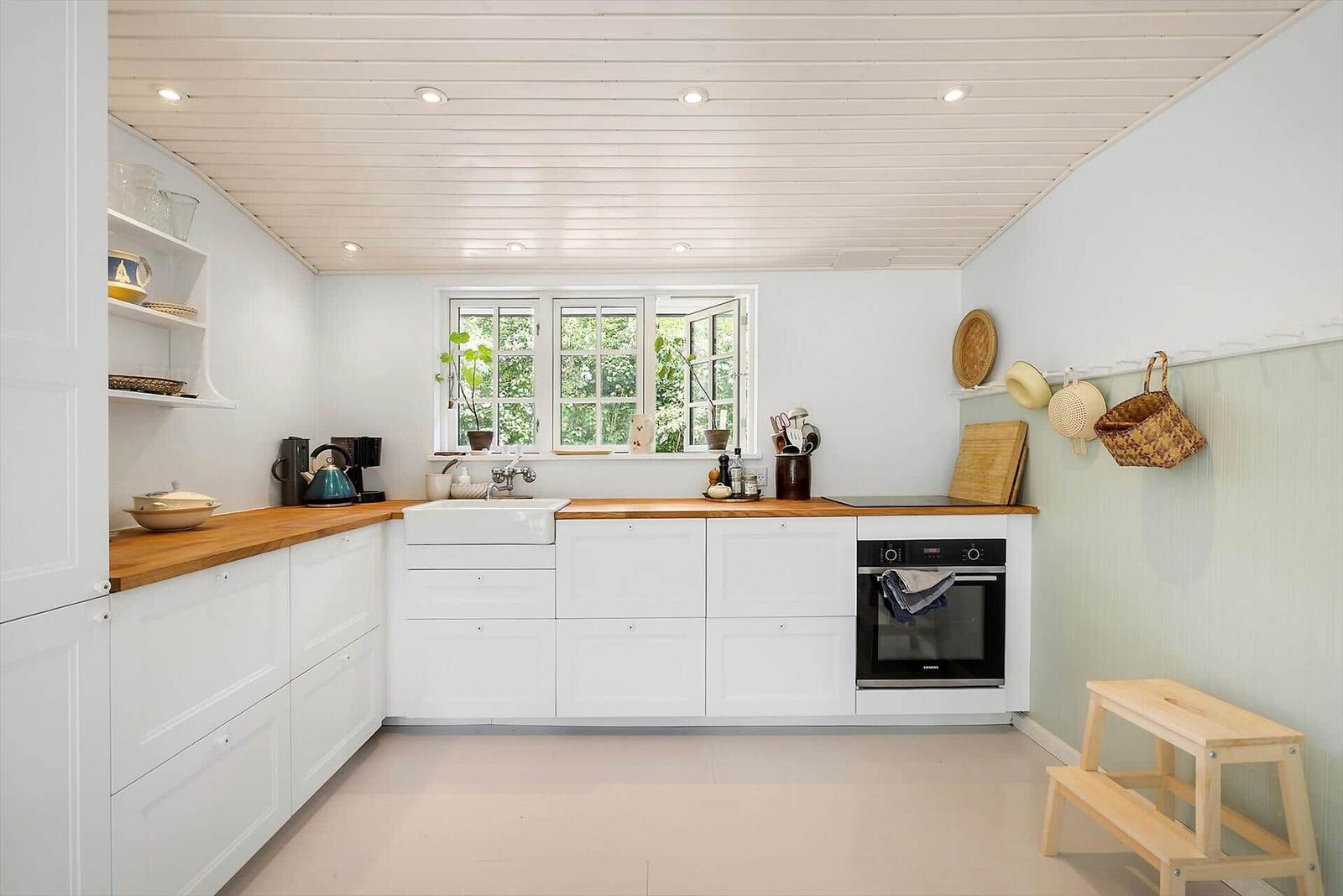 Kitchen with white cabinets, wooden surfaces, and window with view of greenery.