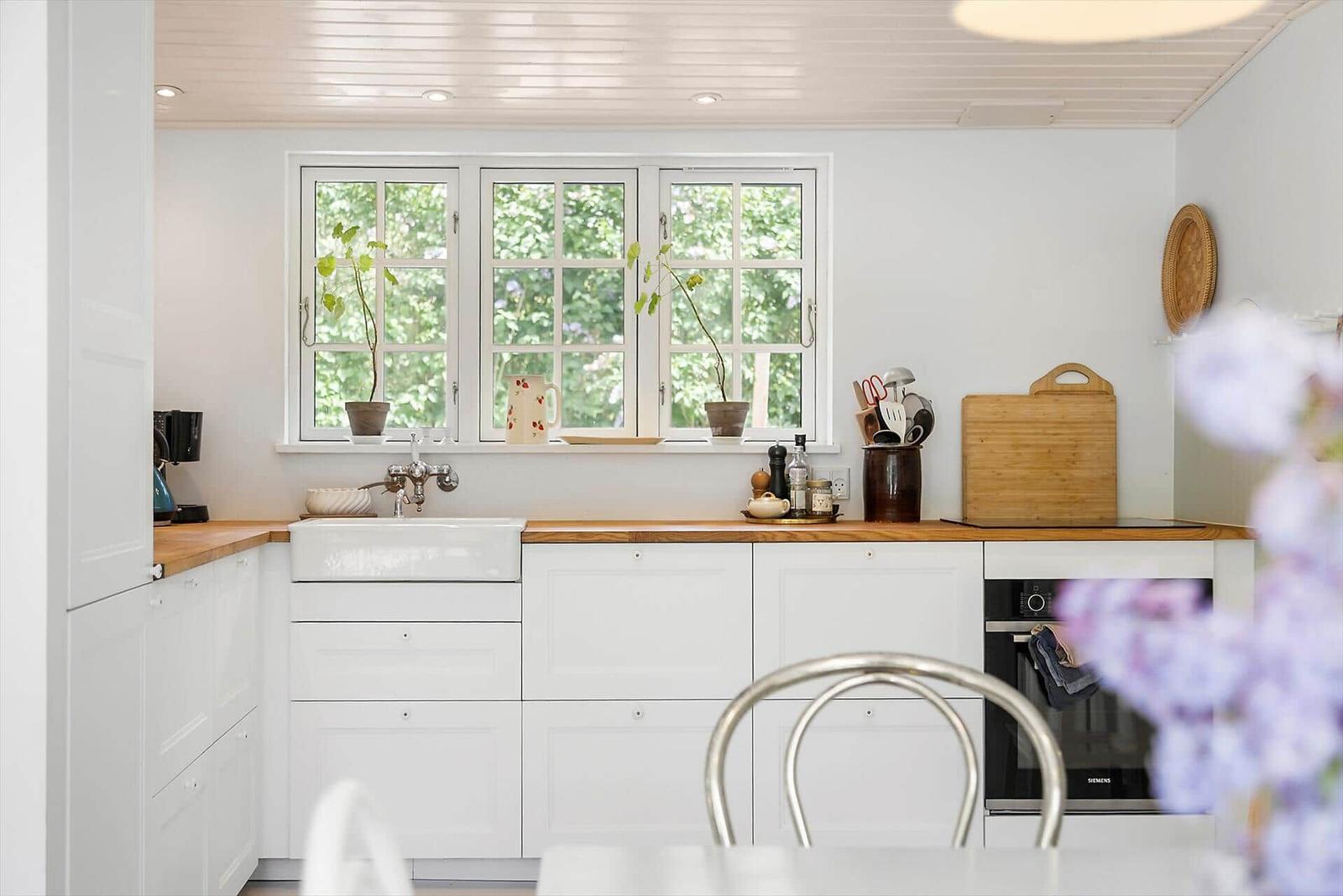 Kitchen with white cabinets, wooden countertop, and windows with plants.