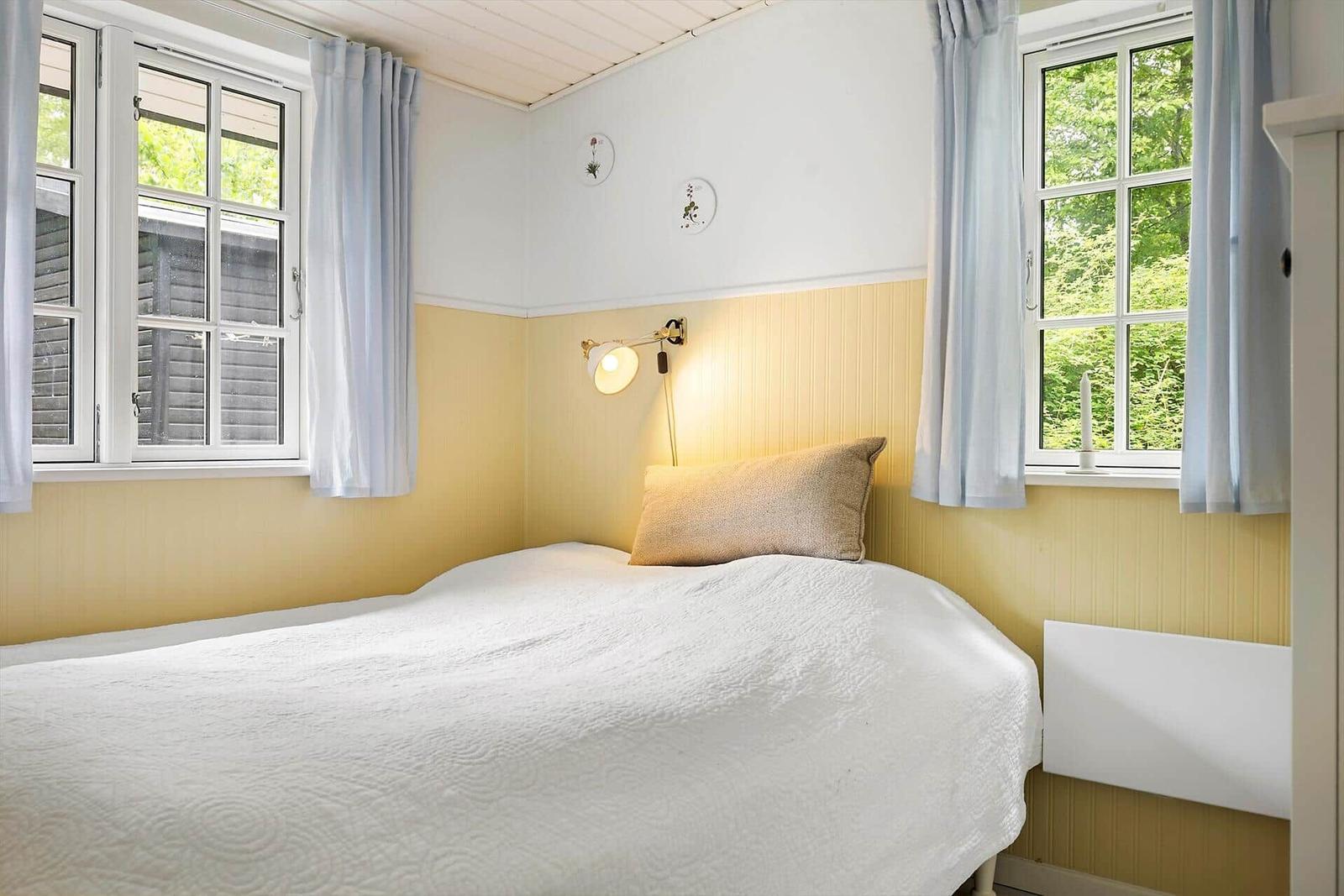 Bedroom with bed, two windows, and yellow wall paneling.