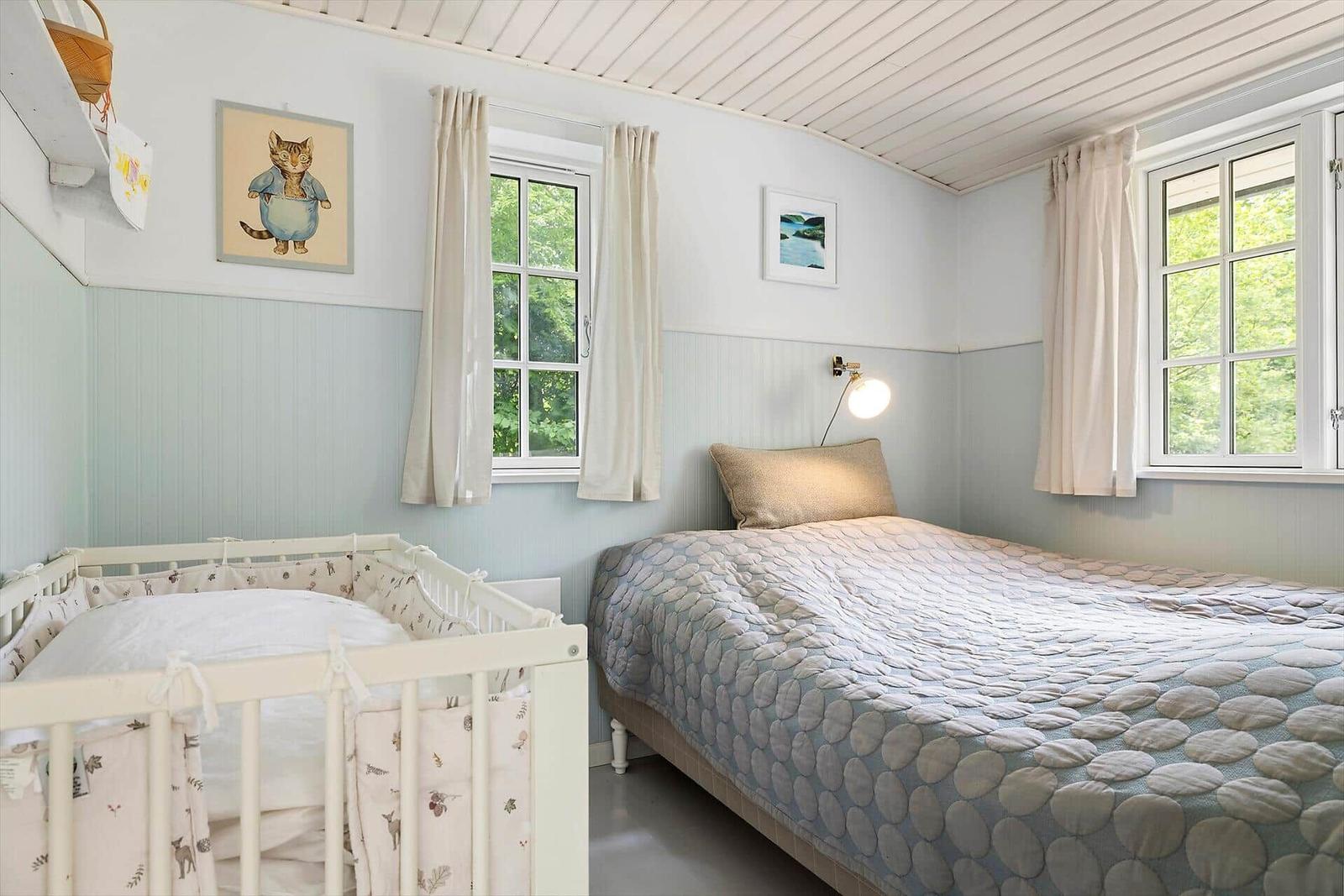 Bedroom with crib and bed. Two windows, white walls and ceiling.