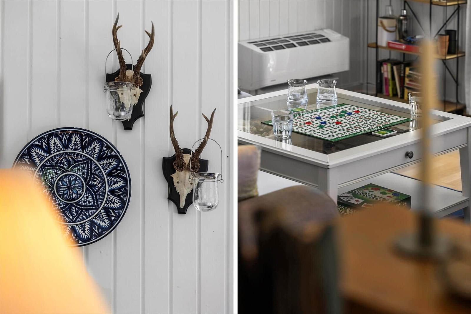 Wand mit Hirschgeweih und blauem Keramikplatten. Tisch mit Spiel und Gläsern.