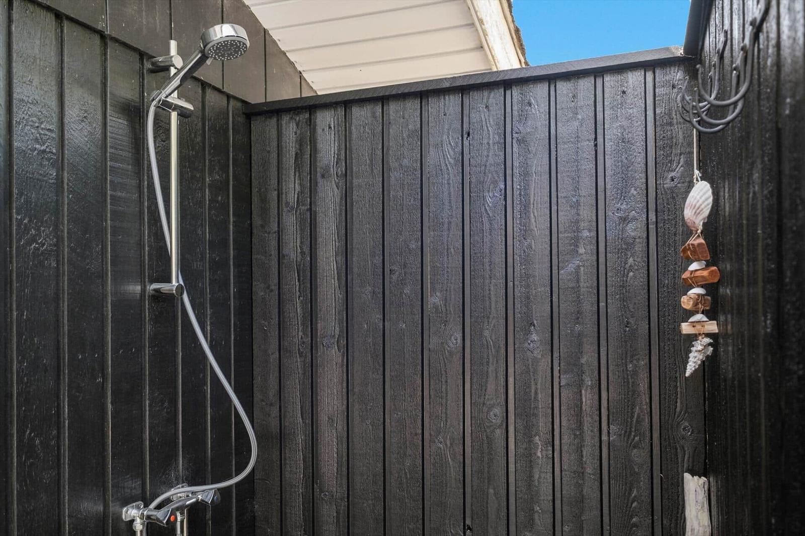 Außen-Dusche mit Duschbrause an schwarzer Holzwand und Meeresmuschel-Dekoration.
