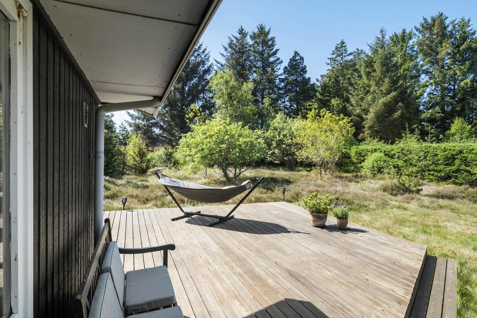 Terrasse mit Hängematte und Sitzbank, umgeben von Wald und Grün.