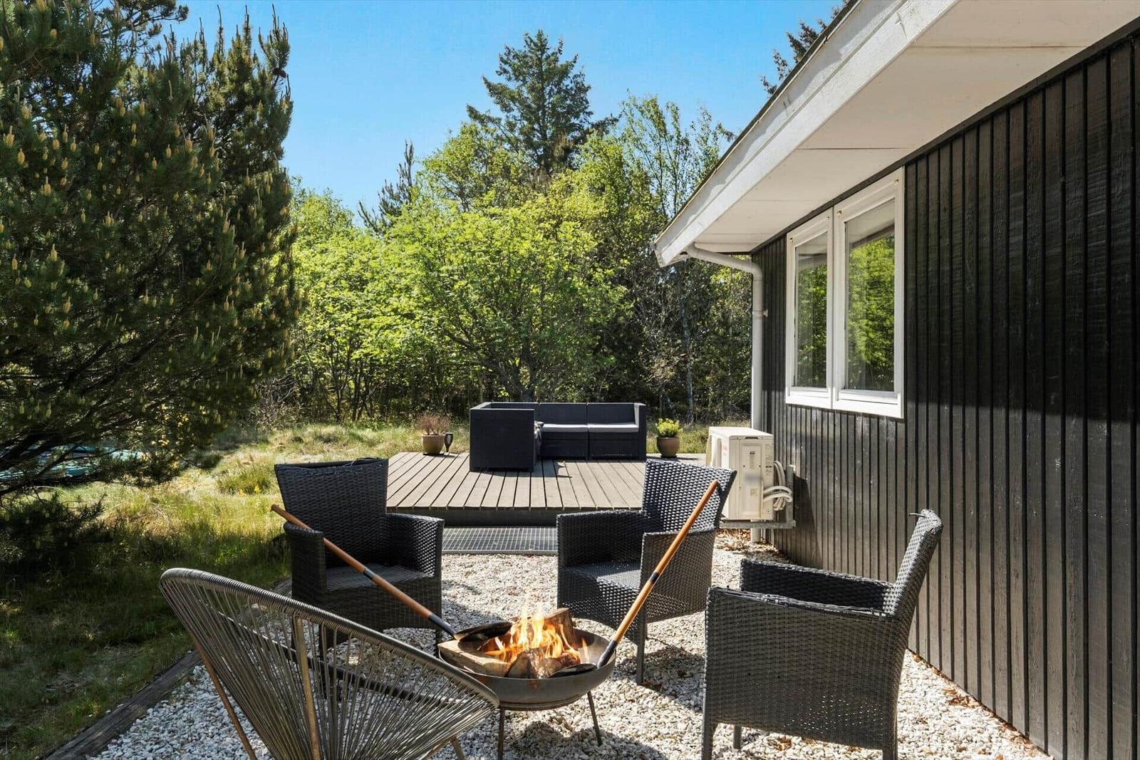 Terrasse mit Sitzgelegenheiten und Kaminfeuer neben einem Haus mit dunkler Fassade.