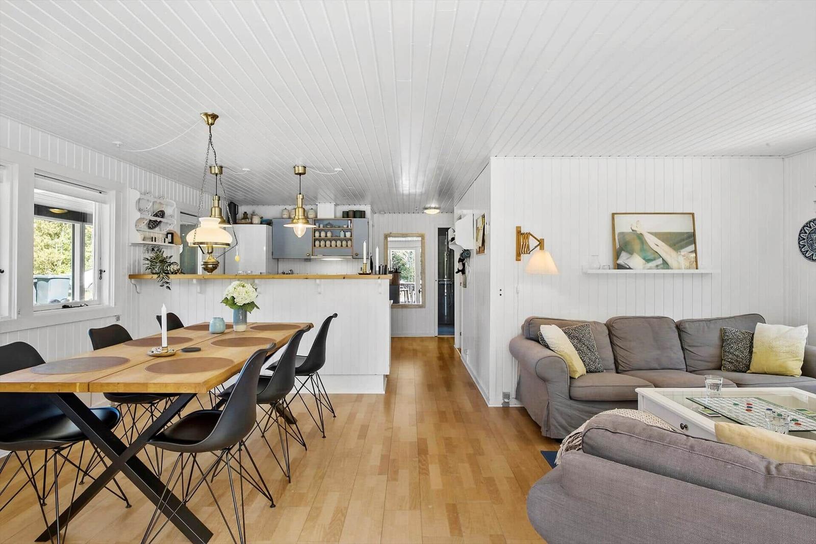 Wohn- und Essbereich mit Kücheninsel, Holzboden und weißer Wandverkleidung.