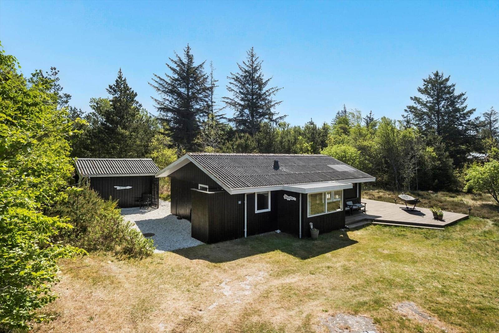 Moderne Holzhütte mit Terrasse und Grillplatz im Wald.
