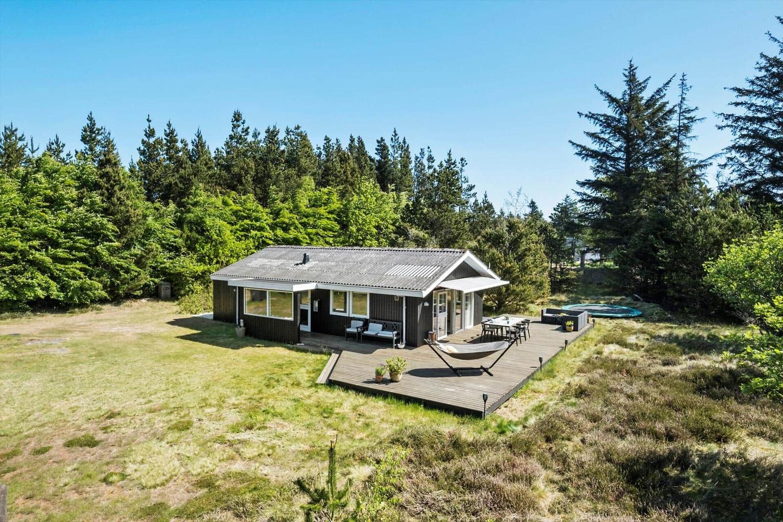 Ein Haus mit Terrasse, Hängematten und Grillplatz inmitten von Bäumen.
