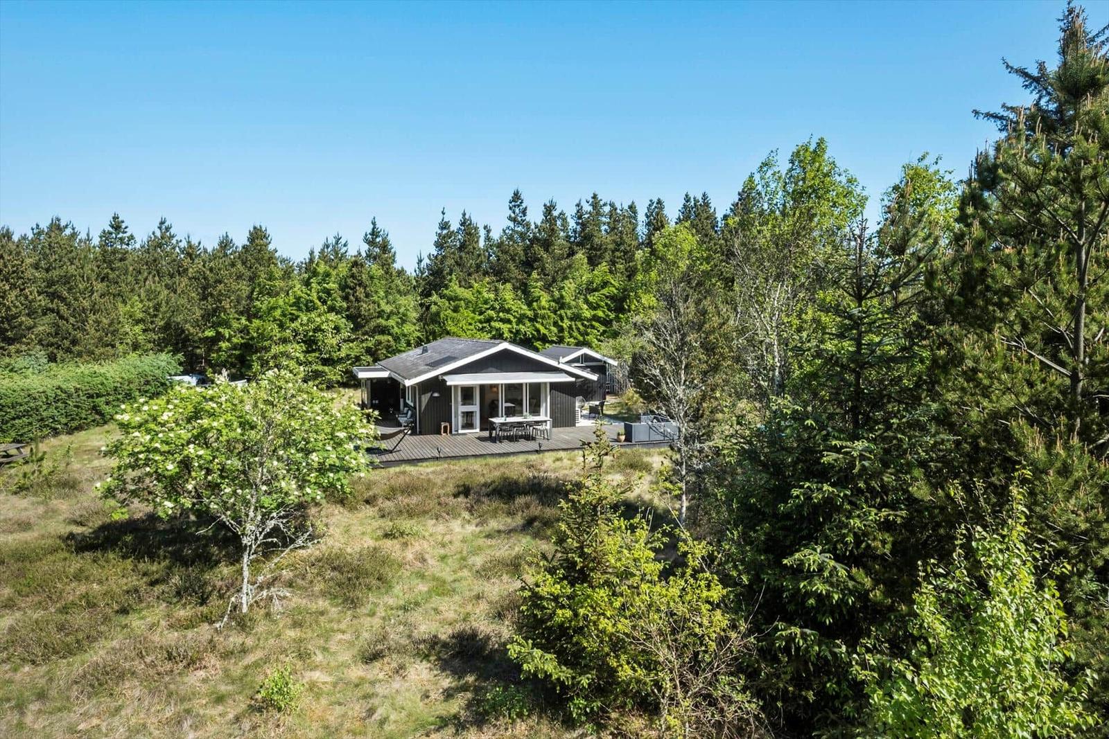 Holzhaus mit Terrasse im Wald, umgeben von Bäumen und Gras.