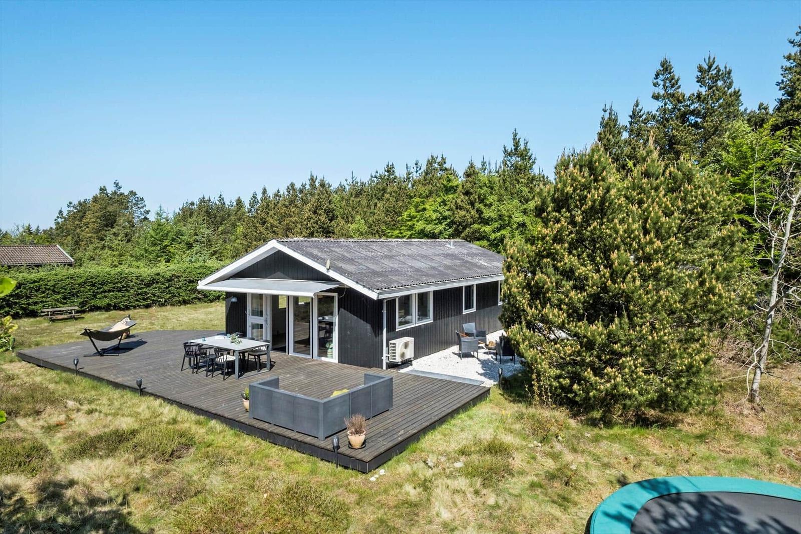 Moderne Ferienhaus mit großem Holzterrasse, Gartenmöbeln und Blick auf Wald.