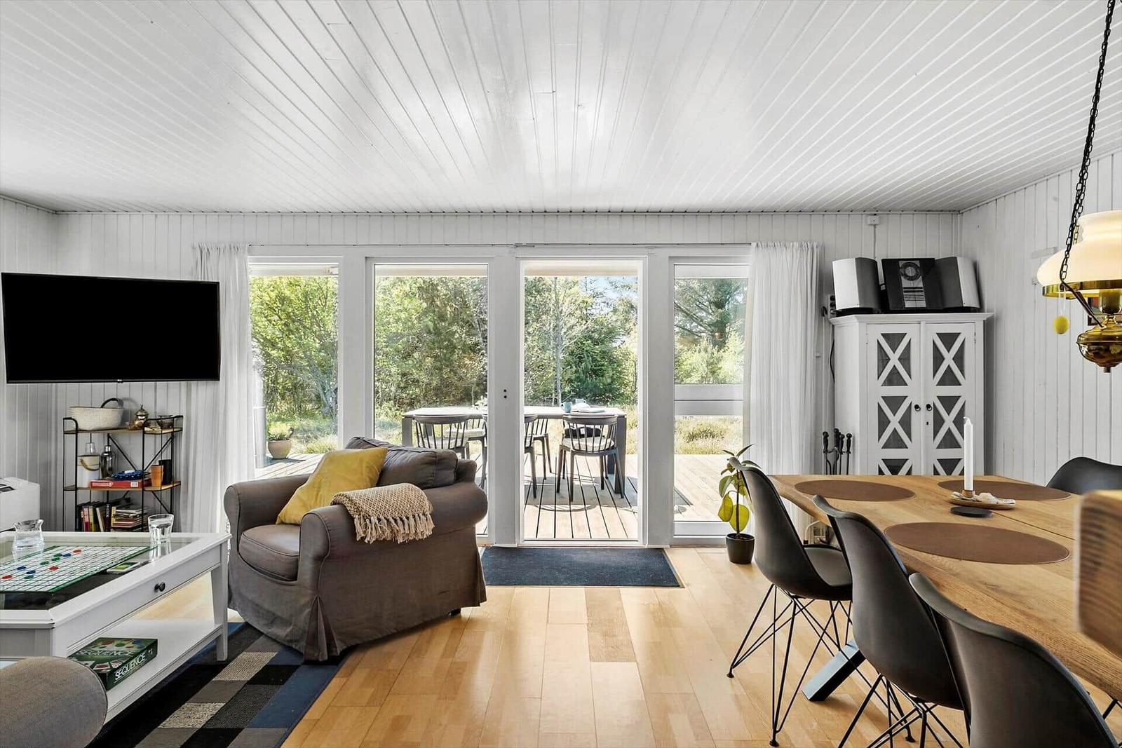 Wohn- und Essbereich mit Holzboden, TV, Sofa und Terrasse.