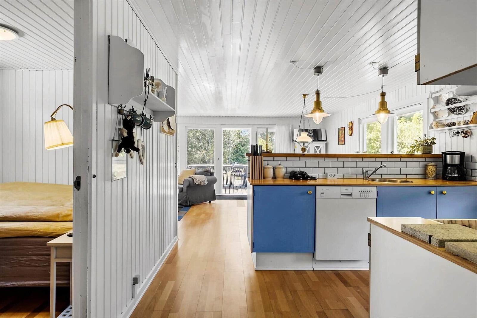 Küche mit blauen Schränken und Holzoberfläche. Im Hintergrund Wohnbereich mit Sofa und Balkon.