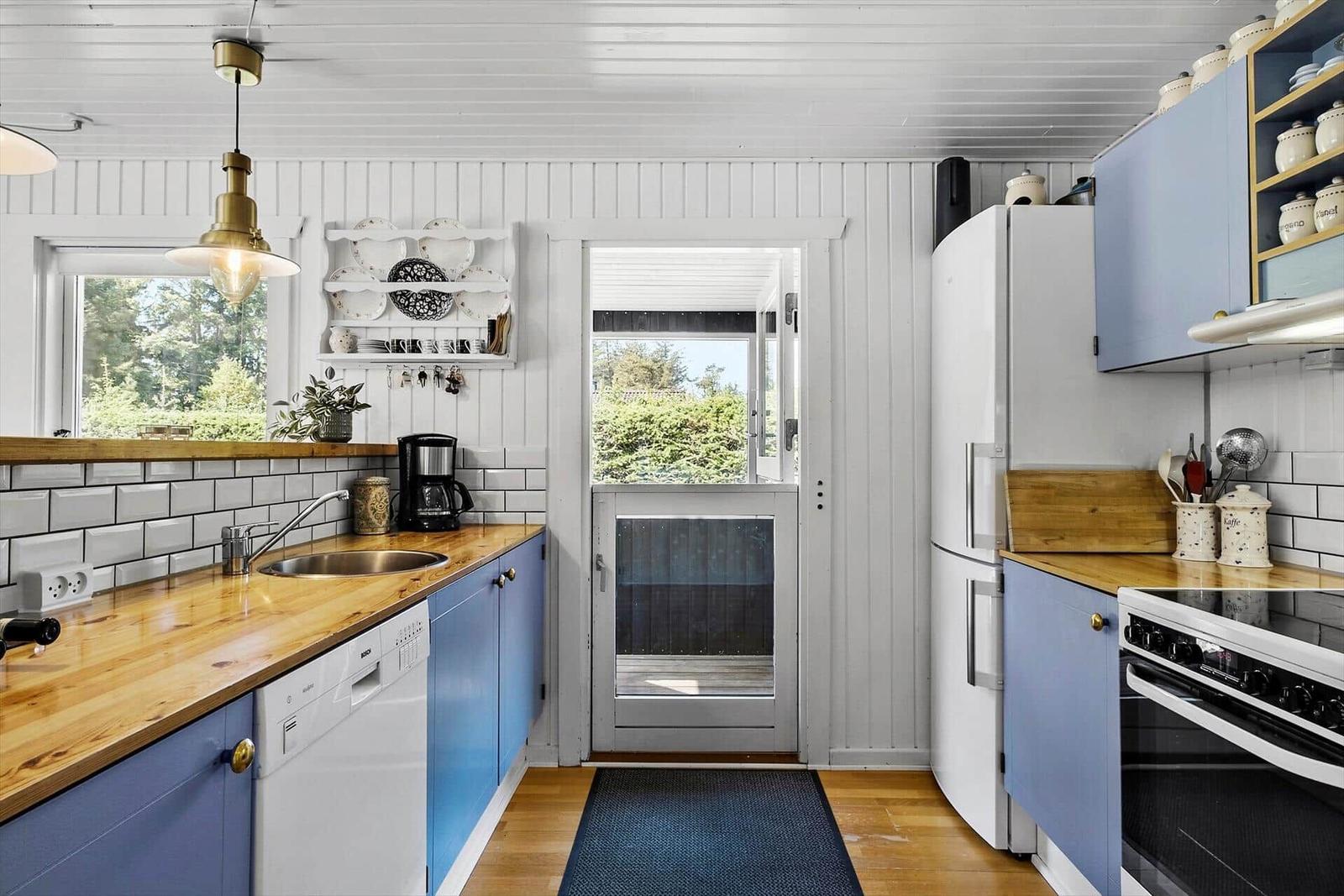 Küche mit blauen Schränken, Holzoberflächen und weißer Kachelwand. Tür führt nach draußen.