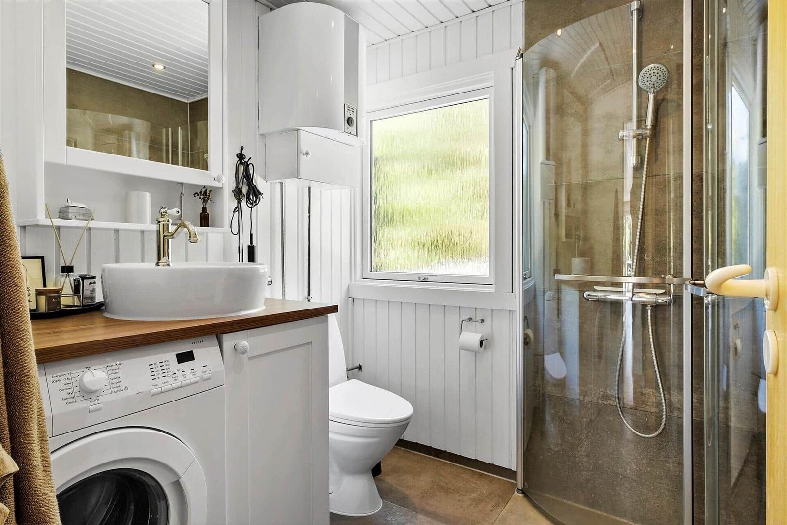 Badezimmer mit Dusche, Waschmaschine und Toilette. Fenster mit Blick auf Gras.