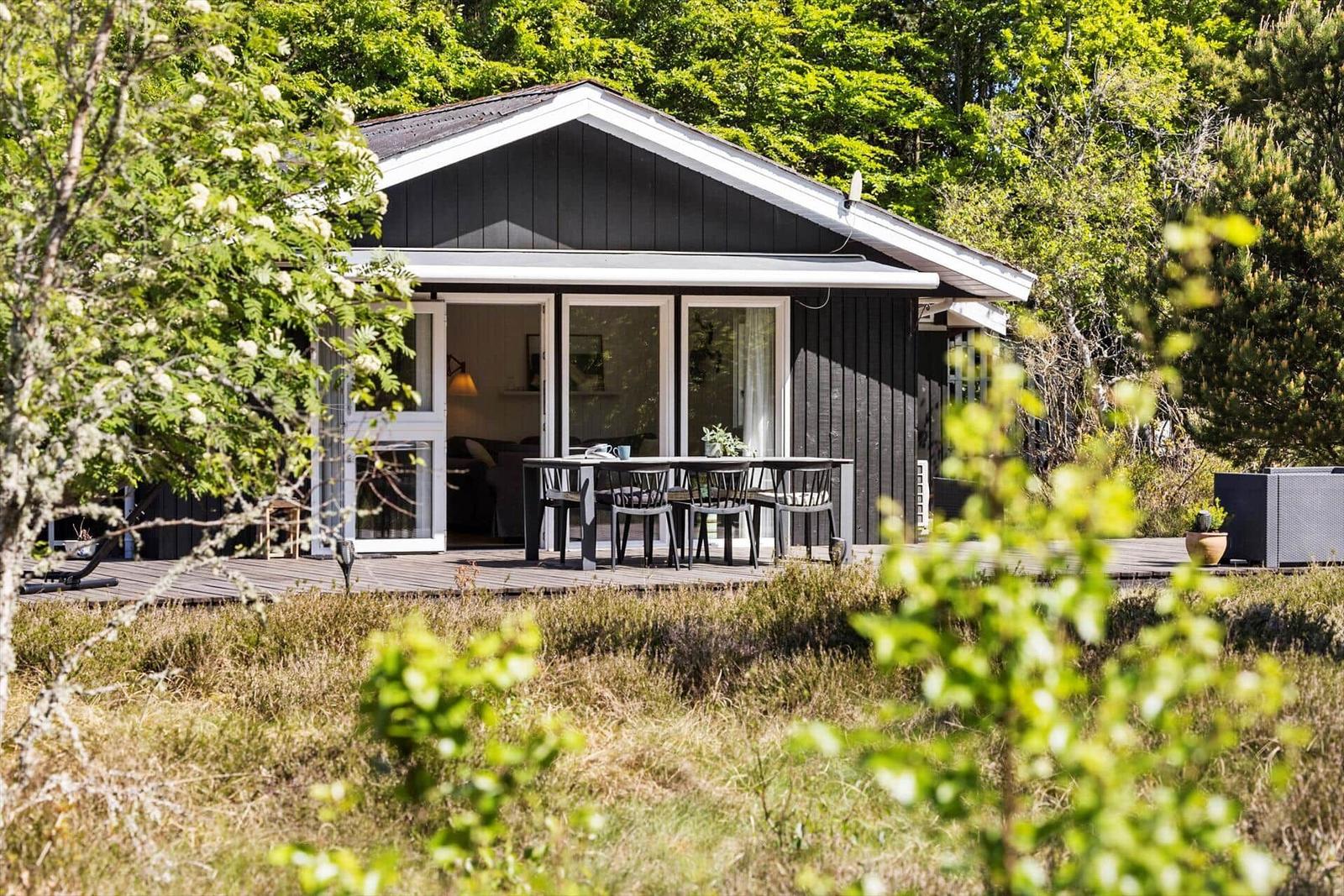 Holzterrasse mit Tisch und Stühlen vor einem Haus mit großem Fensterbereich.