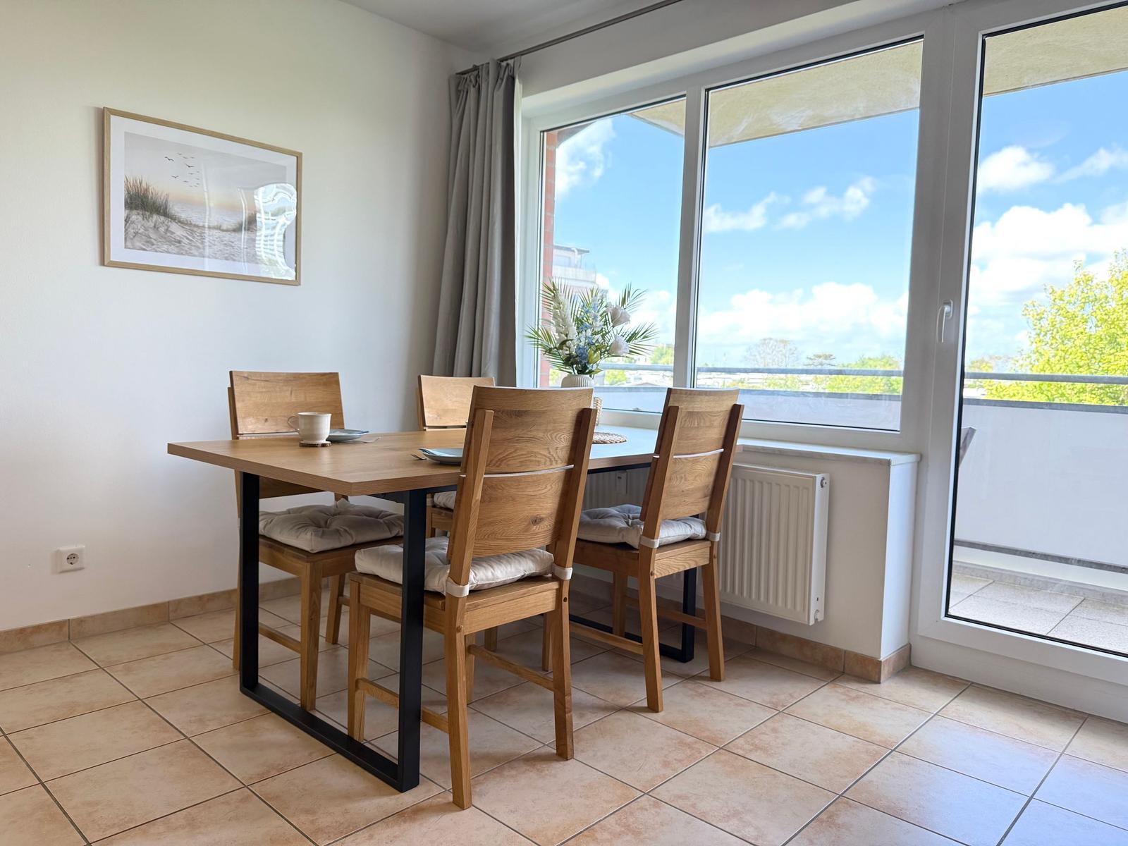 Essbereich mit Holztisch und Stühlen, großes Fenster mit Blick auf Balkon und Himmel.