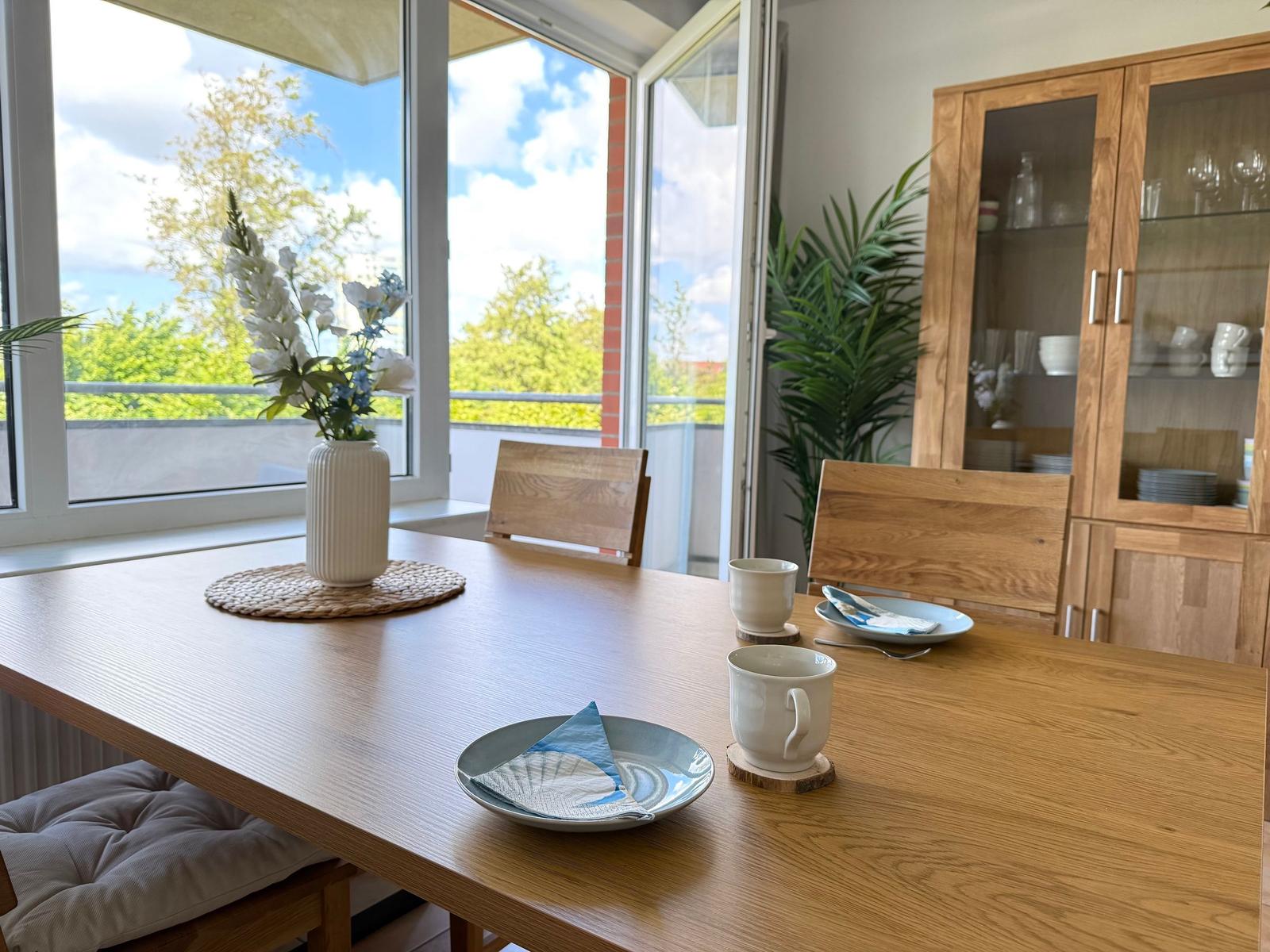 Essbereich mit Holztisch, Stühlen und Blick auf Balkon. Hintergrund: Glaswand und Küchenschränke.