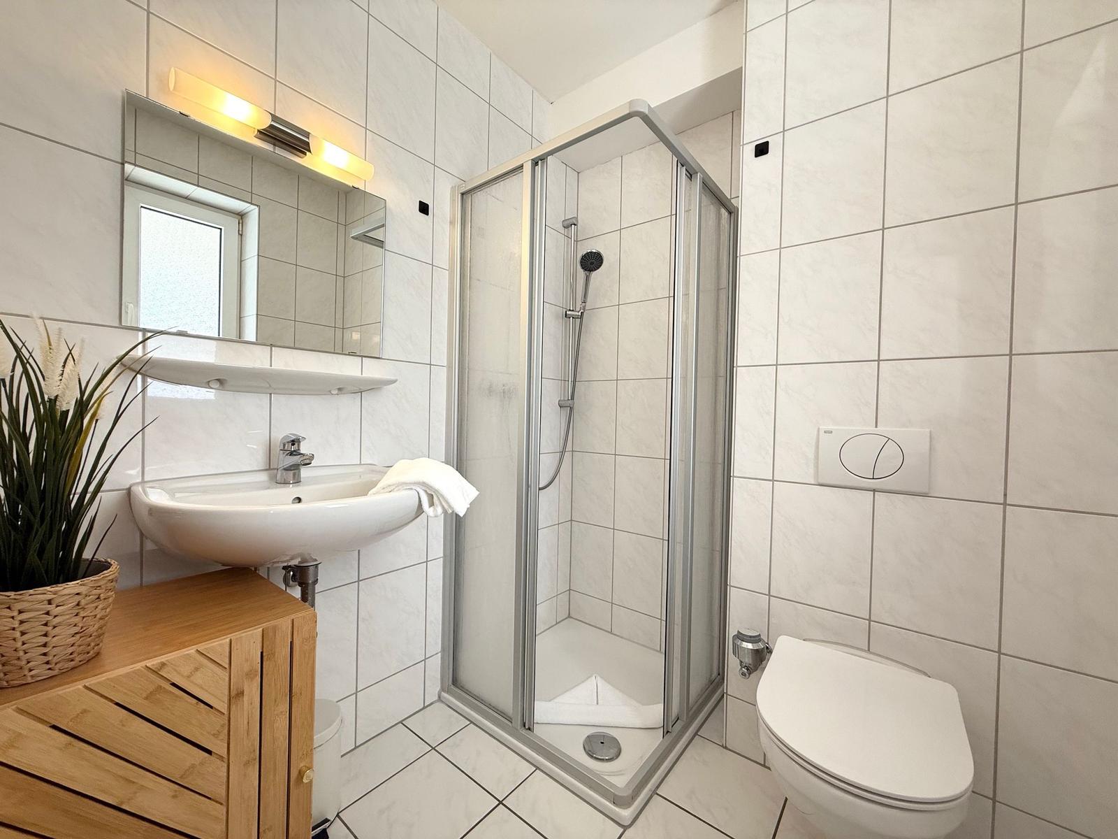 Badezimmer mit Dusche, Waschbecken und Toilette. Holzwaschtisch und Pflanze.