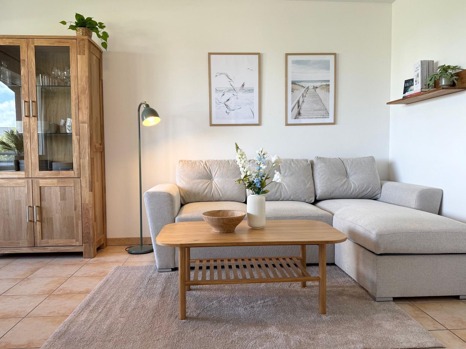 Ein Wohnzimmer mit grauem Sofa, Holztisch und Glasvitrine.