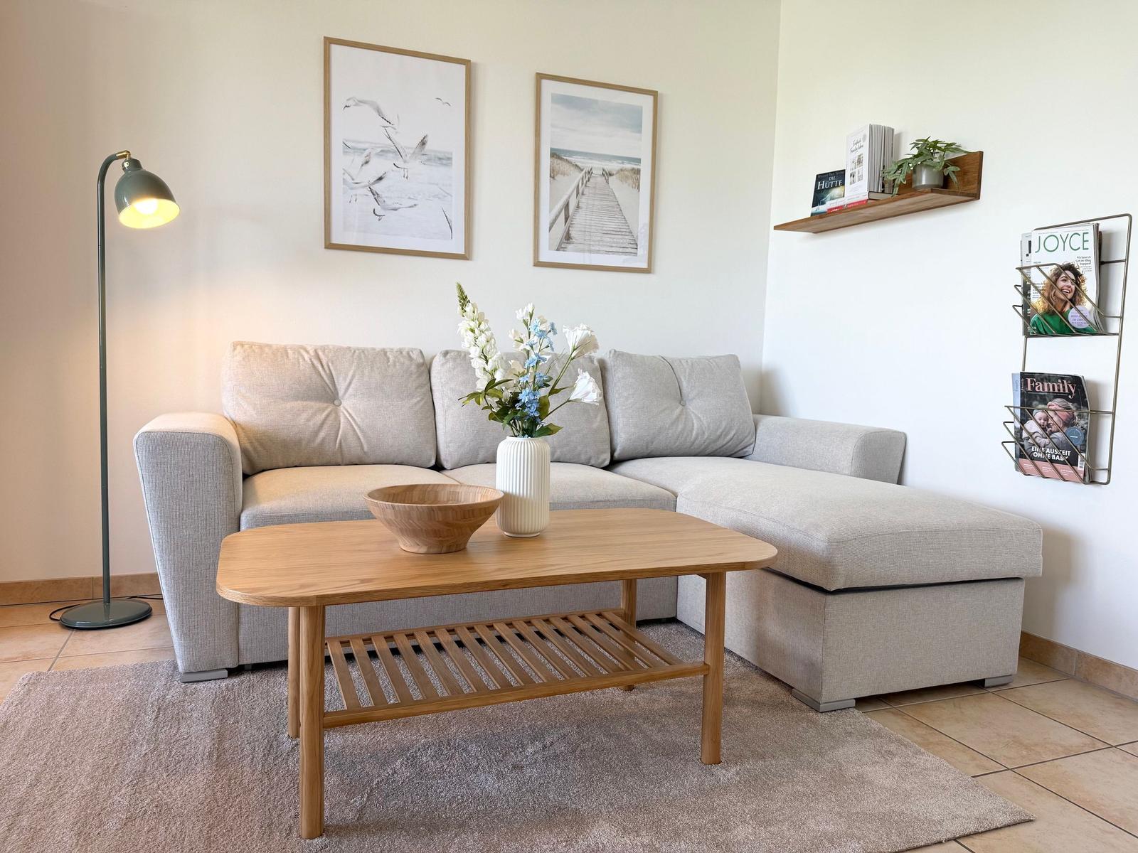 Ein Wohnzimmer mit grauem Sofa, Holztisch und Wandbildern.