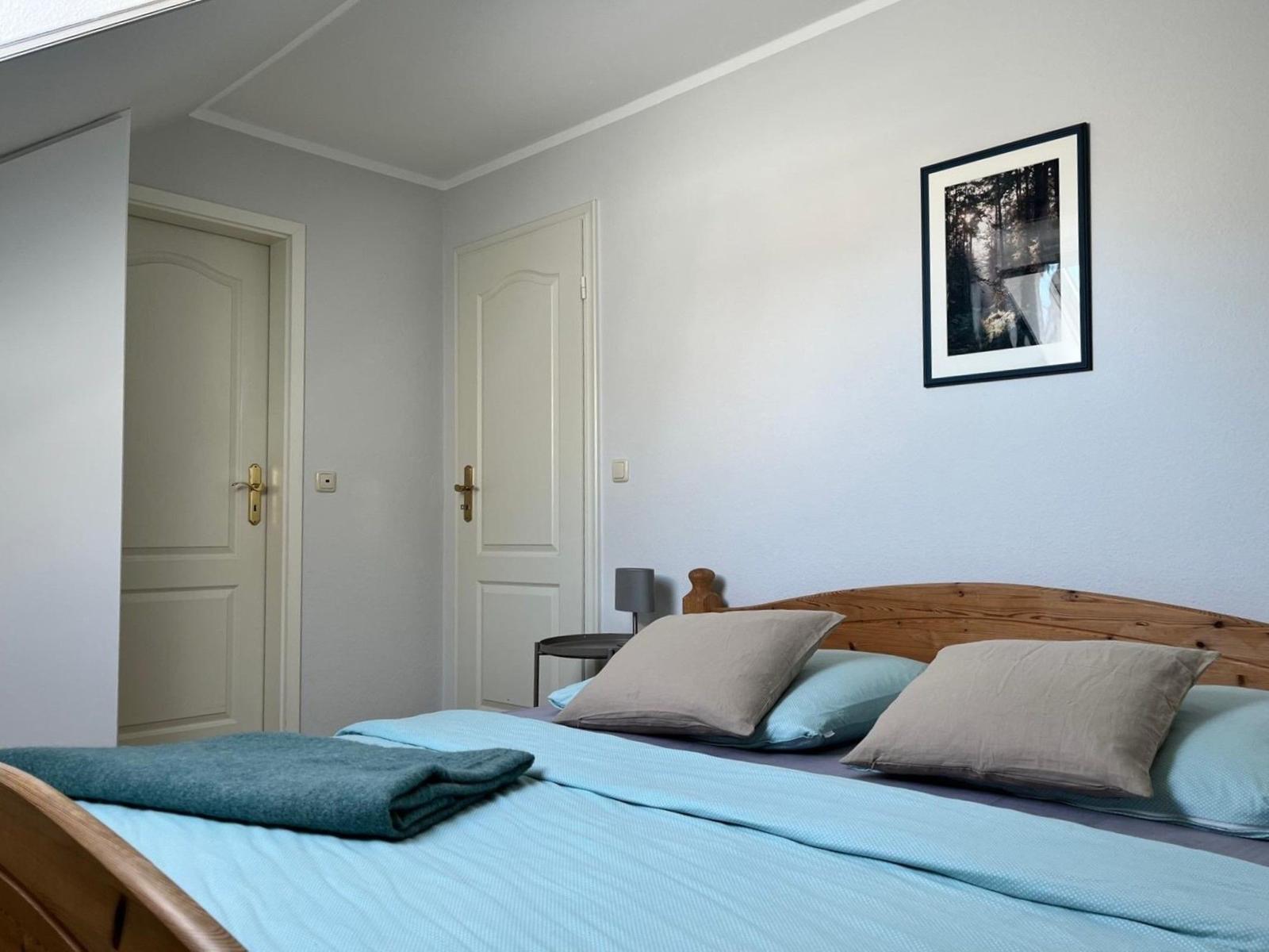 Schlafzimmer mit Holzbett, blauer Bettwäsche und Bild an der Wand.